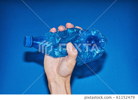 Hand squeezing plastic bottle on blue background. Hand squeezing plastic bottle on blue background. 61152479