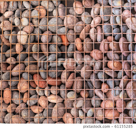 Pebble texture behind lattice. Round pebbles and metal mesh close-up. Unusual background from a grid with stones. Grunge texture. Pebble texture behind lattice. Round pebbles and metal mesh close-up. Unusual background from a grid with stones. Grunge texture. 61155285
