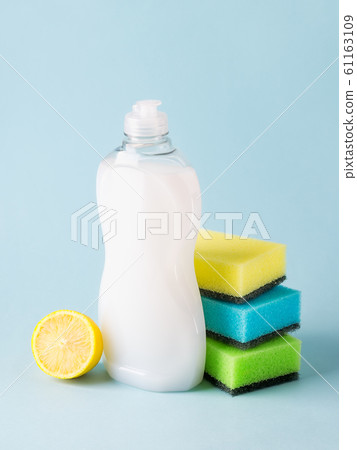 White dishwashing liquid in a plastic bottle, lemon and three foam sponges. 61163109