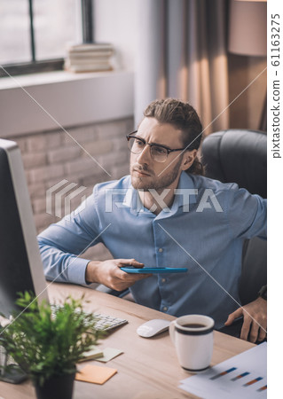 Young bearded man in blue shirt looking attentive Young bearded man in blue shirt looking attentive 61163275