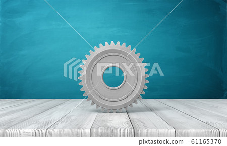 3d rendering of light-grey metal gearwheel standing on wooden surface on blue wall background. 3d rendering of light-grey metal gearwheel standing on wooden surface on blue wall background. 61165370