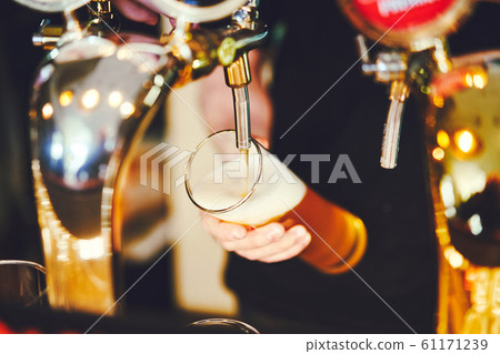the bartender pours beer into a glass from the tap 61171239