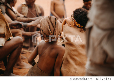 African kid from behind in social group of people sitting in traditional village 61178134