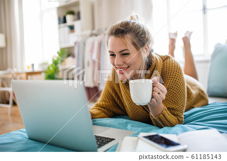 Young woman with laptop lying on bed indoors at home, relaxing. 61185143