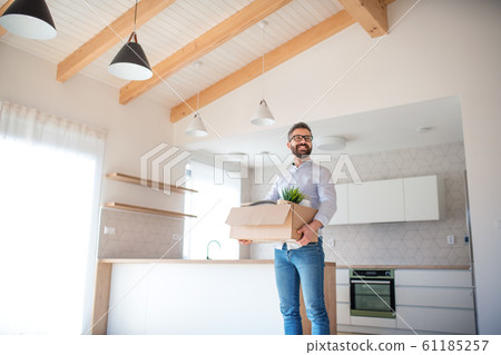 Mature man standing in unfurnished house, holding a moving box. 61185257