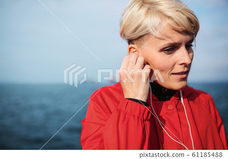 A portrait of young sportswoman with earphones standing outdoors on beach. 61185488