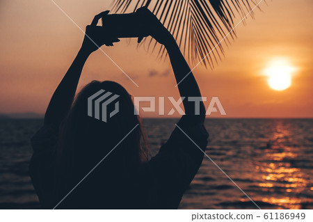 Girl takes a photo on the modern smartphone on the beach. .Silhouette of girl and palm tree on the 61186949