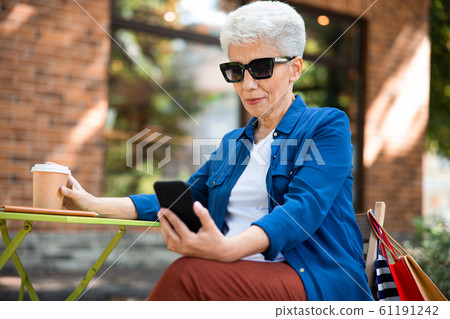 Smiling old woman using mobile phone on the street 61191242