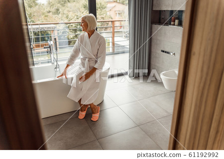 Smiling old woman sitting on the edge of bathtub 61192992