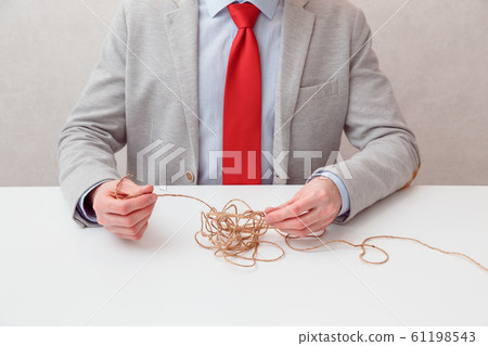Alone businessman try to unwinds tangled thread ball like puzzle out situation. Conceptual photo. 61198543