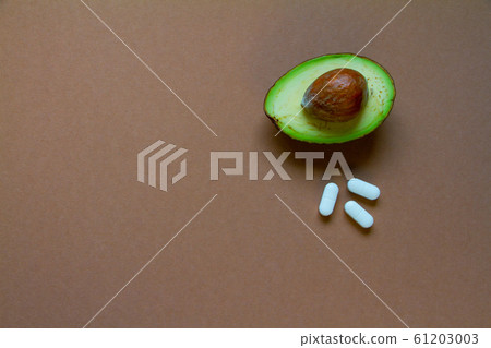 Half of raw avocado and pills on brown background, 61203003