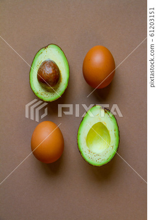Raw two halves of avocado and brown chicken eggs Raw two halves of avocado and brown chicken eggs 61203151