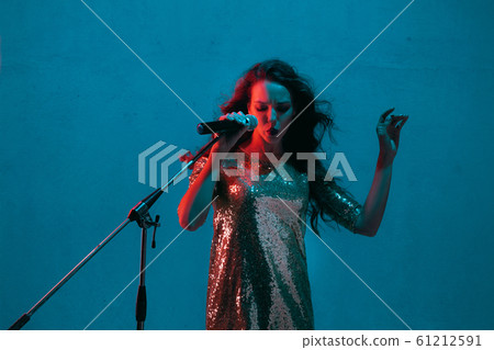Caucasian female singer portrait isolated on blue studio background in neon light Caucasian female singer portrait isolated on blue studio background in neon light 61212591