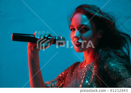 Caucasian female singer portrait isolated on blue studio background in neon light Caucasian female singer portrait isolated on blue studio background in neon light 61212843