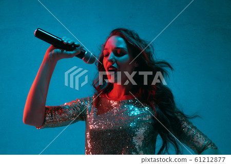 Caucasian female singer portrait isolated on blue studio background in neon light 61212877