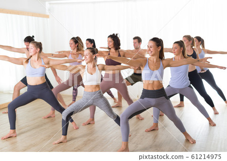 Group of young authentic sporty attractive people in yoga studio, practicing yoga lesson with instructor. Healthy active lifestyle, working out in gym Group of young authentic sporty attractive people in yoga studio, practicing yoga lesson with instructor. Healthy active lifestyle, working out in gym 61214975