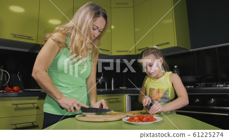 Mother teaching daughter smart girl learning to cook. Mistress children to cook a Neapolitan egg fried omelette from salame affumicato sausage. Mother teaching daughter smart girl learning to cook. Mistress children to cook a Neapolitan egg fried omelette from salame affumicato sausage. 61225274