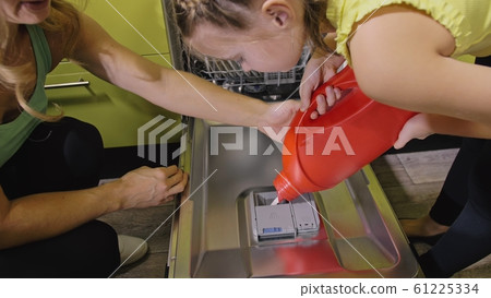 Mother teaching daughter smart girl learning to use dishwasher. Young mistress children loading putting dirty dishes in automatic dishwasher. 61225334