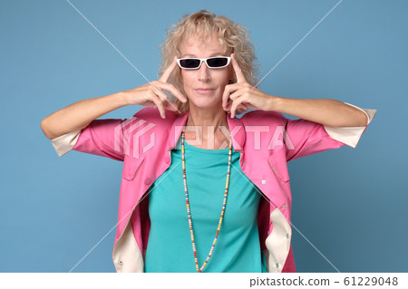 Senior woman wearing stylish sunglasses and smiling at camera on blue wall. Senior woman wearing stylish sunglasses and smiling at camera on blue wall. 61229048