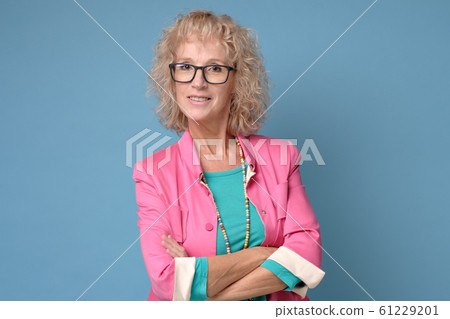 Mature woman with curly blonde hair and glasses smiling and standing confident Mature woman with curly blonde hair and glasses smiling and standing confident 61229201