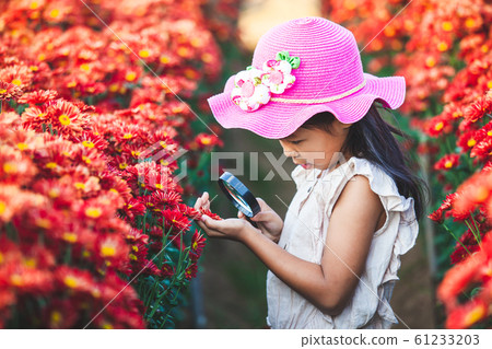 Cute asian child girl looking beautiful flower through a magnifying glass in the flower field 61233203