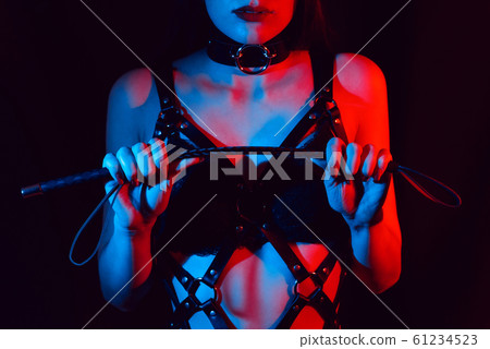 girl in a leather harness holds a Flogger whip in her hands 61234523