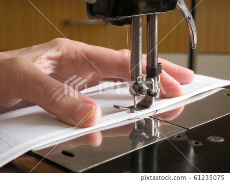 Sewing process. Presser foot, needle bar, fabric feed dog and throat plate of vintage manual tailoring. Human fingers hold a cloth, close up, selected focus. Sewing process. Presser foot, needle bar, fabric feed dog and throat plate of vintage manual tailoring. Human fingers hold a cloth, close up, selected focus. 61235075