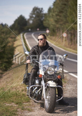 Bearded biker with long hair in black leather jacket sitting on modern motorcycle. Bearded biker with long hair in black leather jacket sitting on modern motorcycle. 61236084
