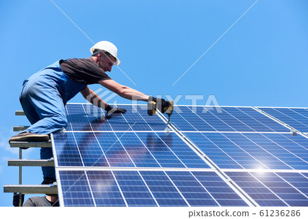 Man mounting modern solar batteries on house's roof. 61236286