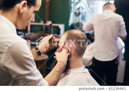Male hairdresser making short haircut for client in modern barbershop. Concept of traditional haircutting with scissors. Male hairdresser making short haircut for client in modern barbershop. Concept of traditional haircutting with scissors. 61236461