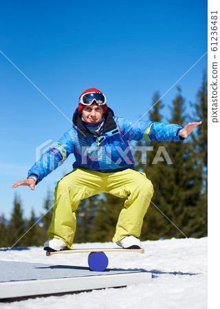 Male snowboarder balancing on snowboard in white snow on background of blue sky and spruce trees. Male snowboarder balancing on snowboard in white snow on background of blue sky and spruce trees. 61236481