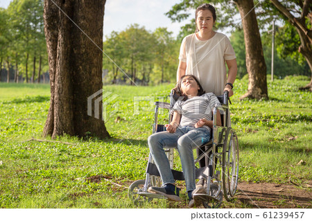 Sick little child girl with cerebral palsy in wheelchair outdoor park or daughter suffering from seizures,illness with epilepsy,asian mother or caregiver care of girl patient,brain,intellectual disabi 61239457