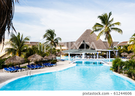 Blue sunbeds under thatch-covered sunshades stand near a swimming pool Blue sunbeds under thatch-covered sunshades stand near a swimming pool 61244606