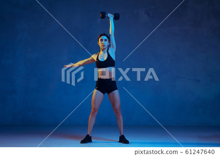 Caucasian young female athlete practicing on blue studio background in neon light Caucasian young female athlete practicing on blue studio background in neon light 61247640