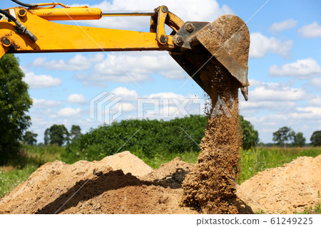 Yellow excavator shovel digging pit in ground 61249225