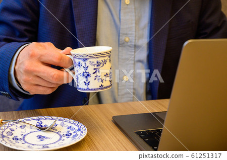 Middle-aged man looking at a computer while drinking 61251317
