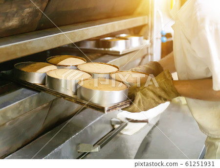 Male cook takes cakes out of a hot oven for making cakes, industry Male cook takes cakes out of a hot oven for making cakes, industry 61251931