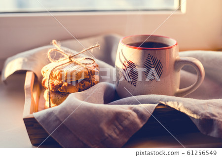 A steaming cup of tea or coffee with cookies by the window. 61256549