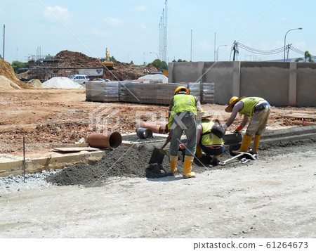 Construction workers creating concrete road curb at the construction site. They are using the in-situ method using the standard metal mold. Construction workers creating concrete road curb at the construction site. They are using the in-situ method using the standard metal mold. 61264673