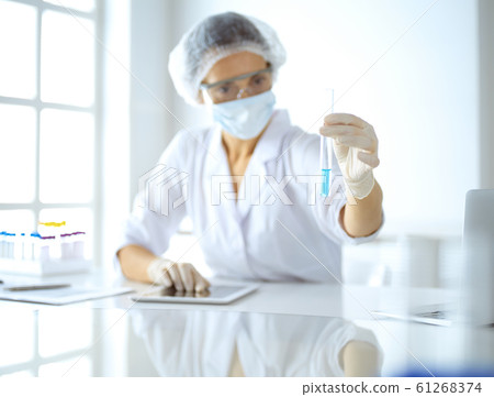 Professional female scientist in protective eyeglasses researching tube with reagents in laboratory. Concepts of medicine and research Professional female scientist in protective eyeglasses researching tube with reagents in laboratory. Concepts of medicine and research 61268374