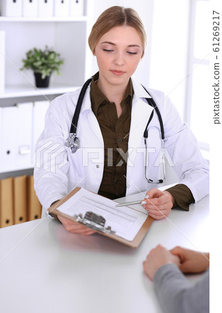 Young woman doctor and patient at medical examination in hospital office. Khaki colored blouse of therapist looks good. Medicine, healthcare and doctor's appointment concept 61269217