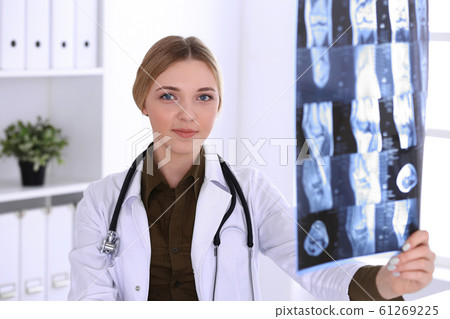 Doctor woman examining x-ray picture near window in hospital. Surgeon or orthopedist at work. Medicine and healthcare concept. Khaki colored blouse of a therapist looks good Doctor woman examining x-ray picture near window in hospital. Surgeon or orthopedist at work. Medicine and healthcare concept. Khaki colored blouse of a therapist looks good 61269225