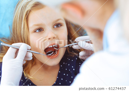 Little baby girl sitting at dental chair with open mouth during oral check up while doctor. Visiting dentist office. Medicine concept. Toned photo Little baby girl sitting at dental chair with open mouth during oral check up while doctor. Visiting dentist office. Medicine concept. Toned photo 61274437