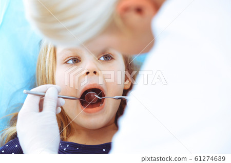 Little baby girl sitting at dental chair with open mouth during oral check up while doctor. Visiting dentist office. Medicine concept. Toned photo Little baby girl sitting at dental chair with open mouth during oral check up while doctor. Visiting dentist office. Medicine concept. Toned photo 61274689