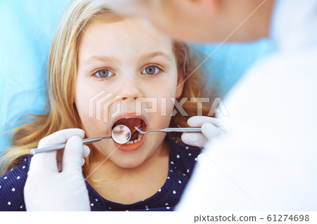 Little baby girl sitting at dental chair with open mouth during oral check up while doctor. Visiting dentist office. Medicine concept. Toned photo Little baby girl sitting at dental chair with open mouth during oral check up while doctor. Visiting dentist office. Medicine concept. Toned photo 61274698