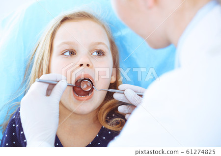 Little baby girl sitting at dental chair with open mouth during oral check up while doctor. Visiting dentist office. Medicine concept. Toned photo Little baby girl sitting at dental chair with open mouth during oral check up while doctor. Visiting dentist office. Medicine concept. Toned photo 61274825