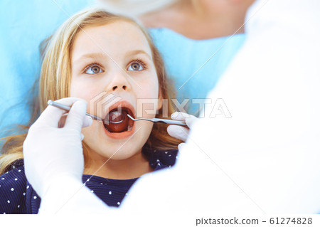 Little baby girl sitting at dental chair with open mouth during oral check up while doctor. Visiting dentist office. Medicine concept. Toned photo Little baby girl sitting at dental chair with open mouth during oral check up while doctor. Visiting dentist office. Medicine concept. Toned photo 61274828