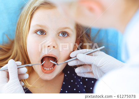 Little baby girl sitting at dental chair with open mouth during oral check up while doctor. Visiting dentist office. Medicine concept. Toned photo Little baby girl sitting at dental chair with open mouth during oral check up while doctor. Visiting dentist office. Medicine concept. Toned photo 61275078