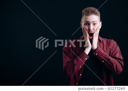 A Surprised Young Man Touching His Cheeks A Surprised Young Man Touching His Cheeks 61277260