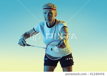 Senior woman playing badminton in sportwear on gradient background in neon light Senior woman playing badminton in sportwear on gradient background in neon light 61280456